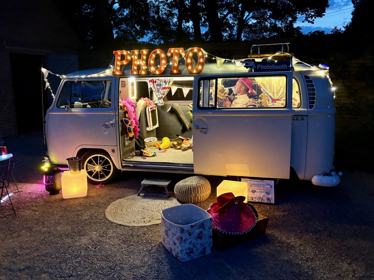 Campervan photo booth wedding hire A vintage camper van decorated with lights, surrounded by colourful props for a photo booth.