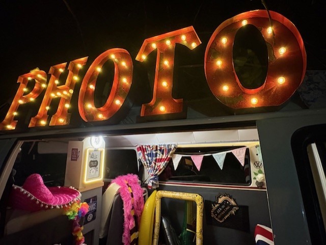 Neon photobooth sign Brightly lit "PHOTO" sign atop a decorated van with vibrant props and bunting.